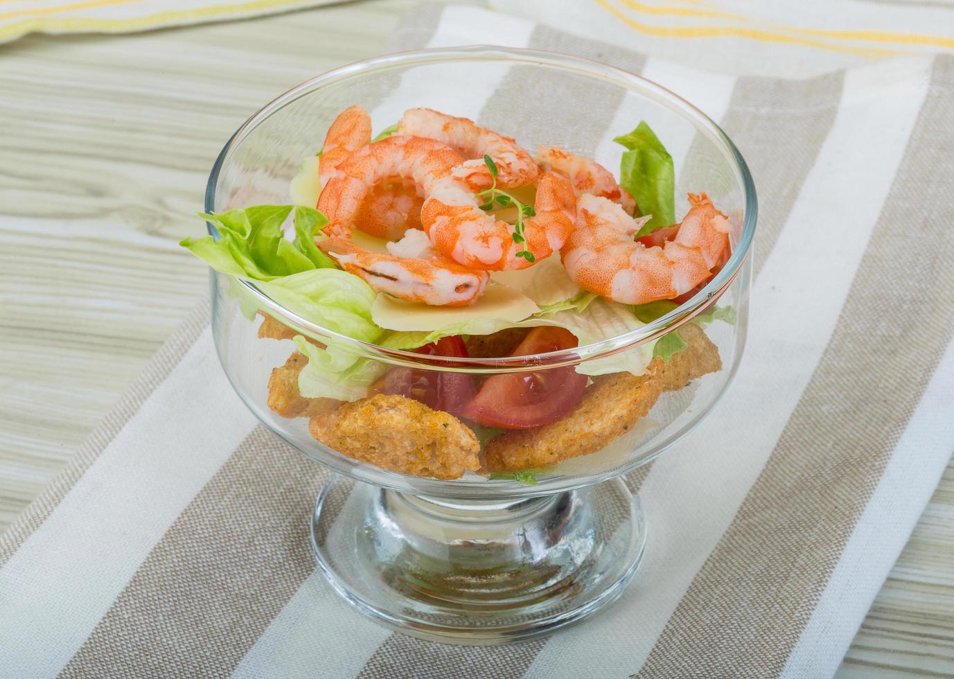 Caesar salad with shrimps in a bowl on wooden background photo