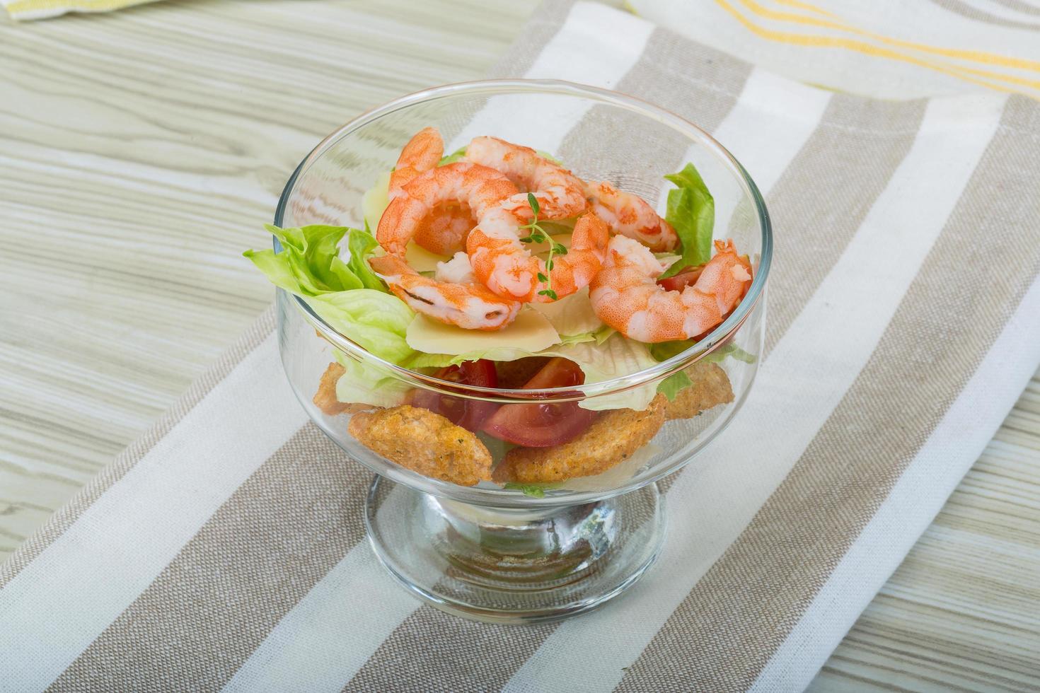 Caesar salad with shrimps in a bowl on wooden background photo