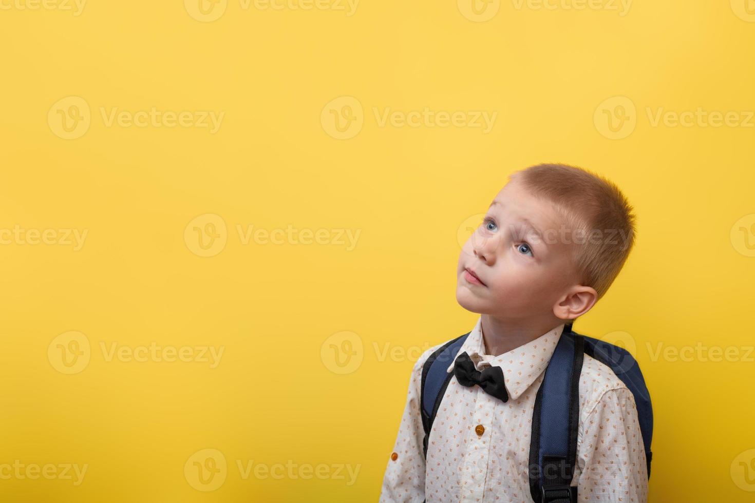 Back to school. A blond boy with a backpack in a light shirt on a yellow background looks up. Copy space. Education. Banner photo
