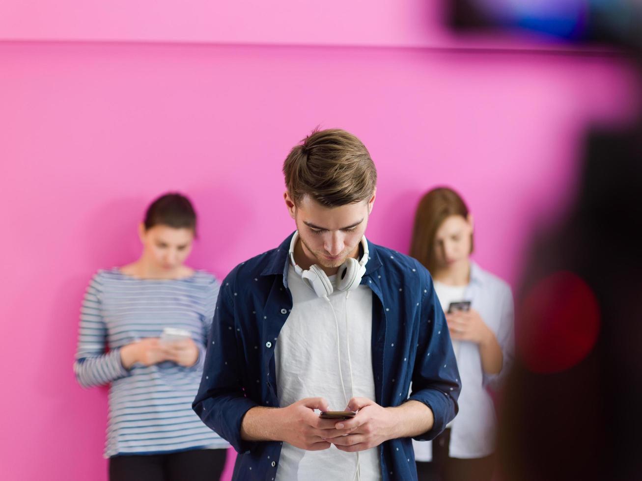 group of diverse teenagers use mobile devices while posing for studio photo