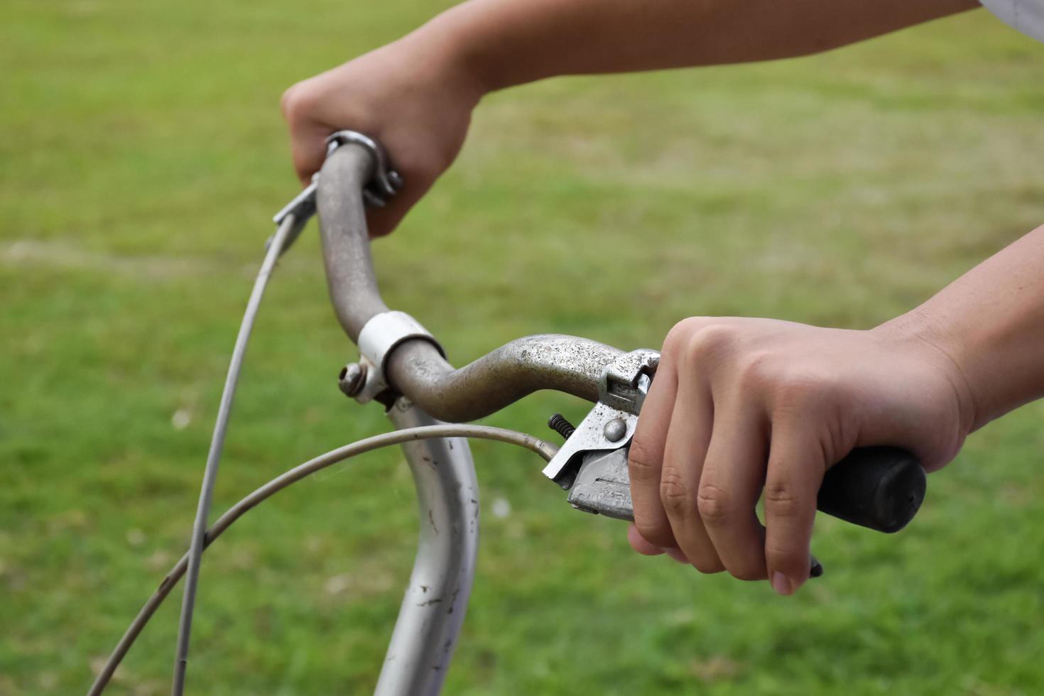 A young guy holds handle bars of vintage bike which parked on the meadow background, soft and selective focus on hand. photo