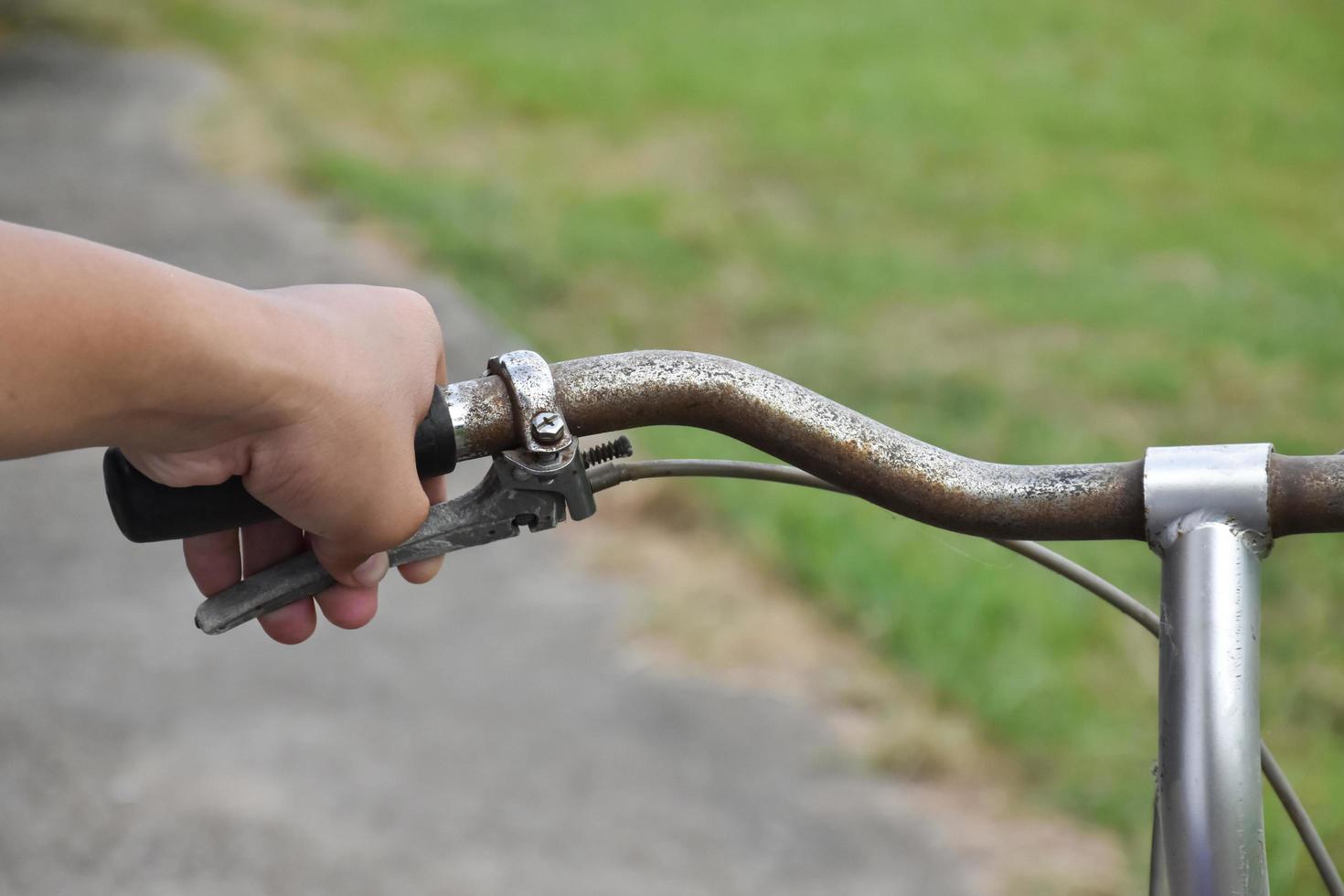 A young guy holds handle bars of vintage bike which parked on the meadow background, soft and selective focus on hand. photo