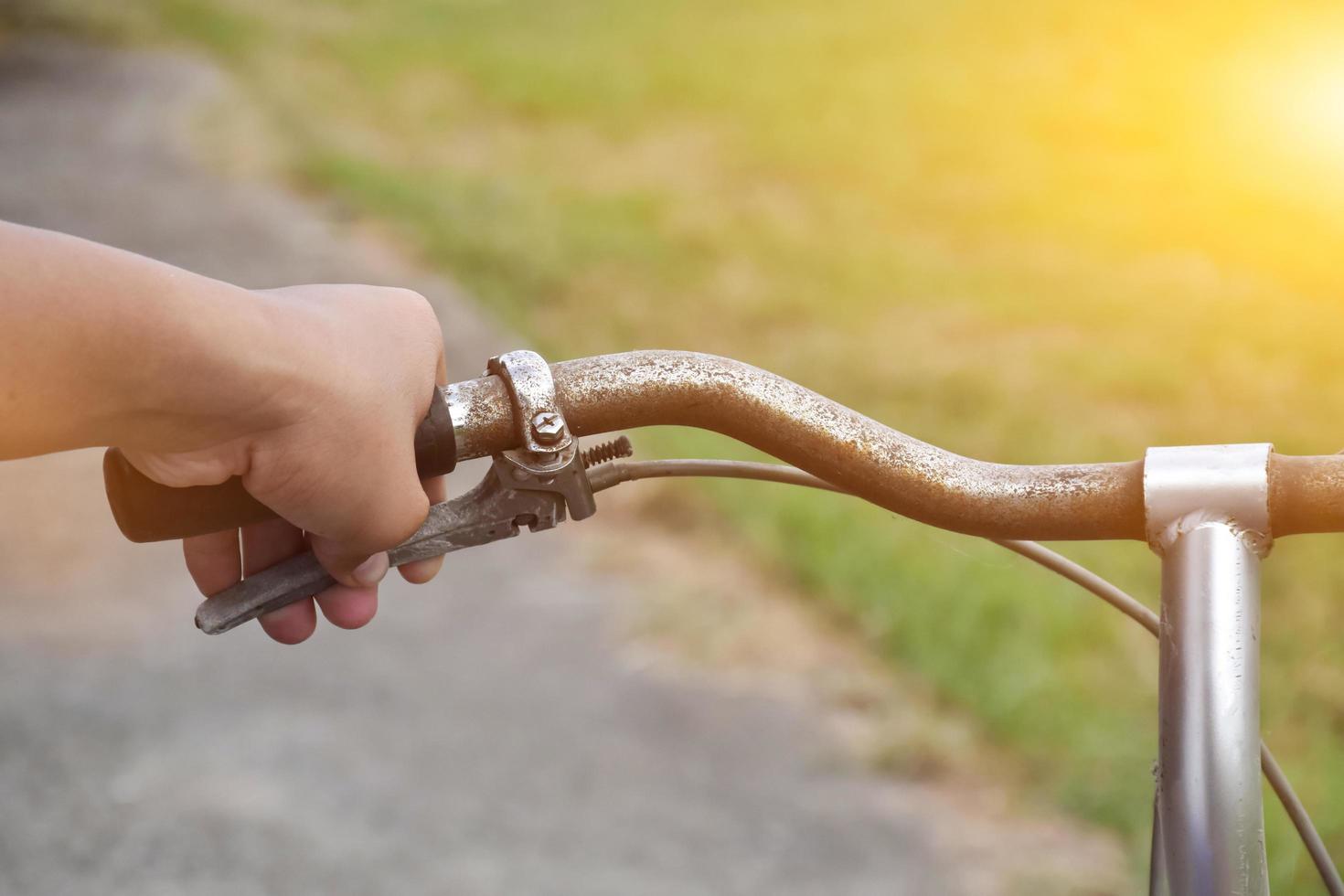 A young guy holds handle bars of vintage bike which parked on the meadow background, soft and selective focus on hand. photo