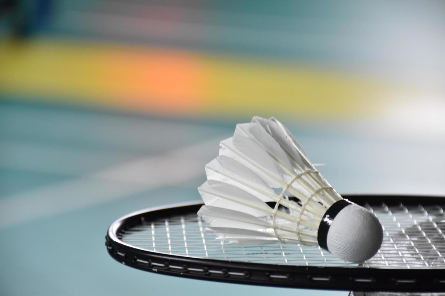 volante de bádminton blanco crema y raqueta con sombreado de luz de neón en el suelo verde en la cancha de bádminton cubierta, fondo de bádminton borroso, espacio para copiar. foto