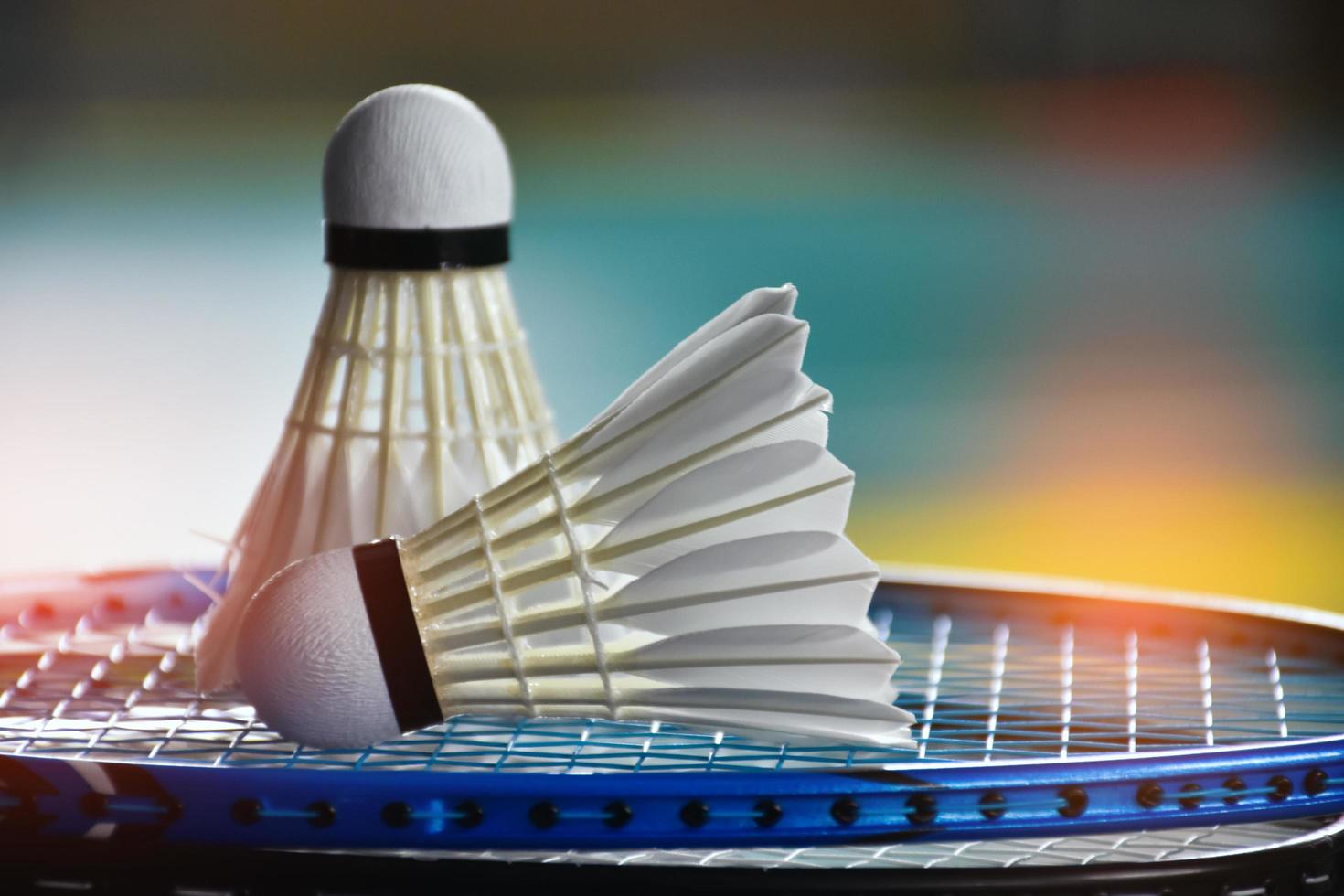 Cream white badminton shuttlecock and racket with neon light shading on green floor in indoor badminton court, blurred badminton background, copy space. photo