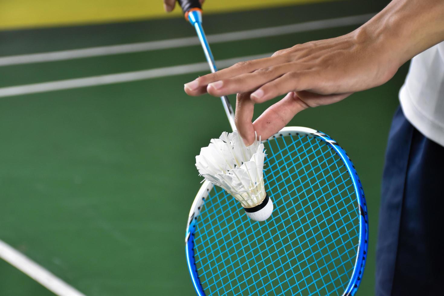 Badminton player holds racket and white cream shuttlecock in front of the net before serving it to another side of the court. photo