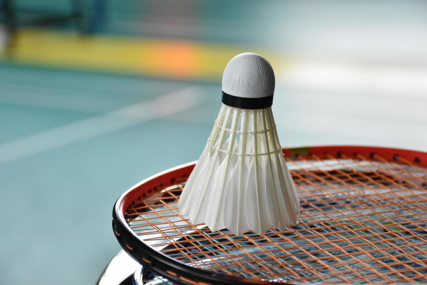 Cream white badminton shuttlecock and racket with neon light shading on green floor in indoor badminton court, blurred badminton background, copy space. photo