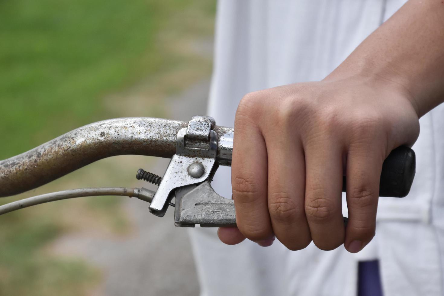 A young guy holds handle bars of vintage bike which parked on the meadow background, soft and selective focus on hand. photo