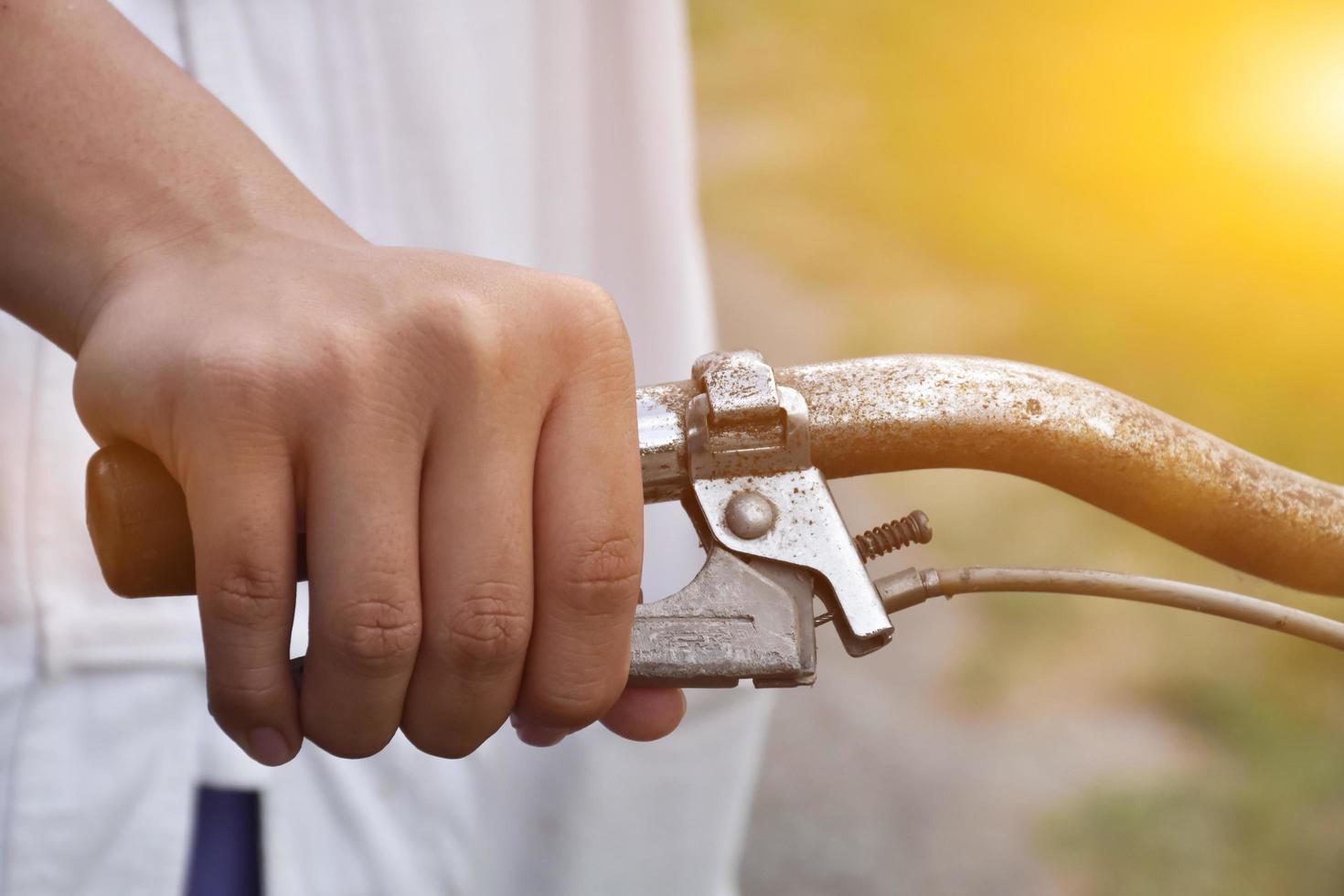 A young guy holds handle bars of vintage bike which parked on the meadow background, soft and selective focus on hand. photo