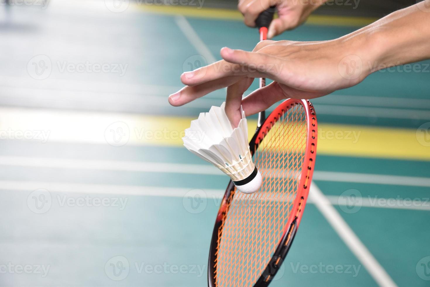 Badminton player holds racket and white cream shuttlecock in front of the net before serving it to another side of the court. photo