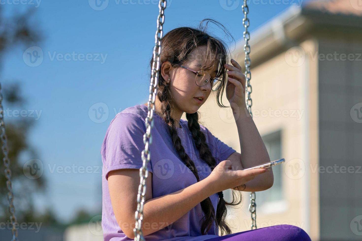 a teenager girl swings on a swing with a phone in her hands, communicates in social networks or learns online photo