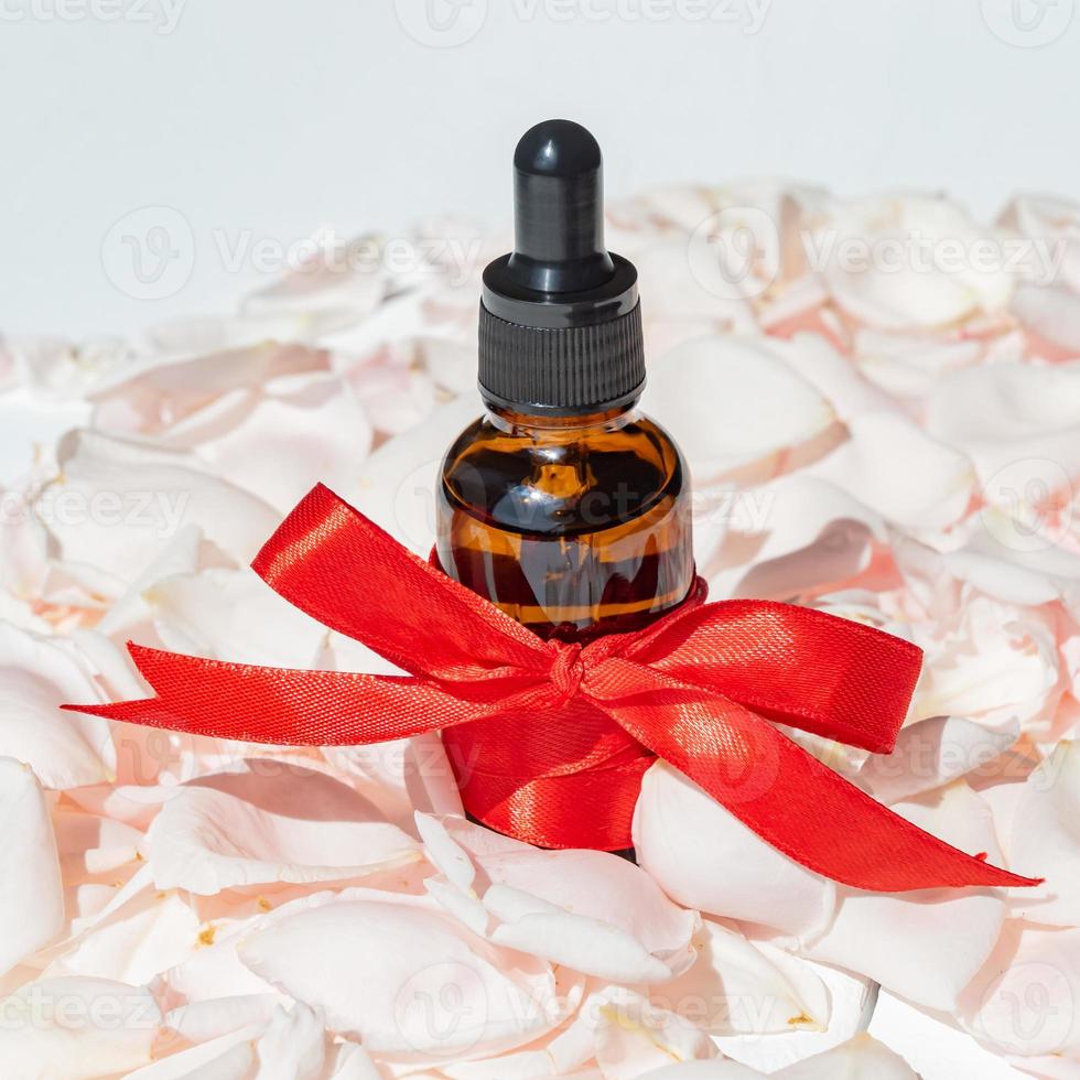 Face serum in a glass package, bottle on a pink rose petals background. treatment for skin with oils, vitamins and collagen. Packaging of cosmetic beauty product photo