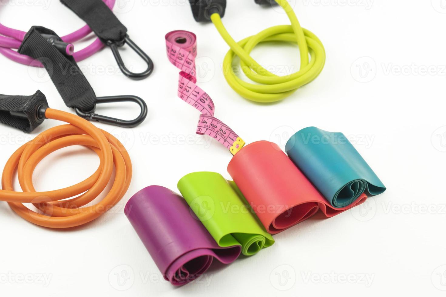 Colorful fitness elastic bands and expanders, a pink measuring tape lie on a white floor photo