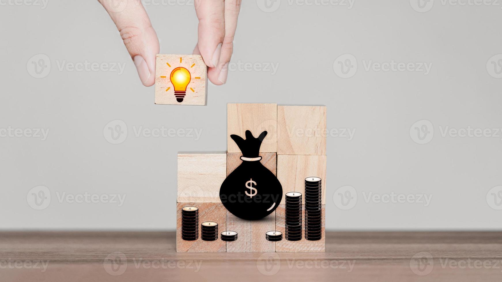 Adding business ideas to make money from online stores. Hand holding light bulb creative icon on wooden cube block with money icon. Business growth idea. photo