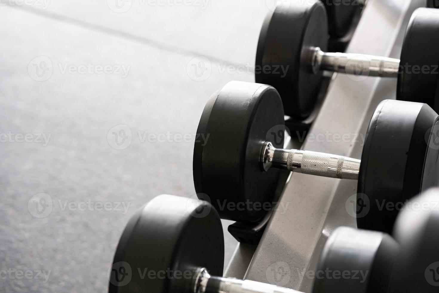 pararse con pesas. Sala de deportes y fitness. equipo de entrenamiento con pesas. juego de mancuernas negras, muchas mancuernas en el rack en el gimnasio deportivo foto