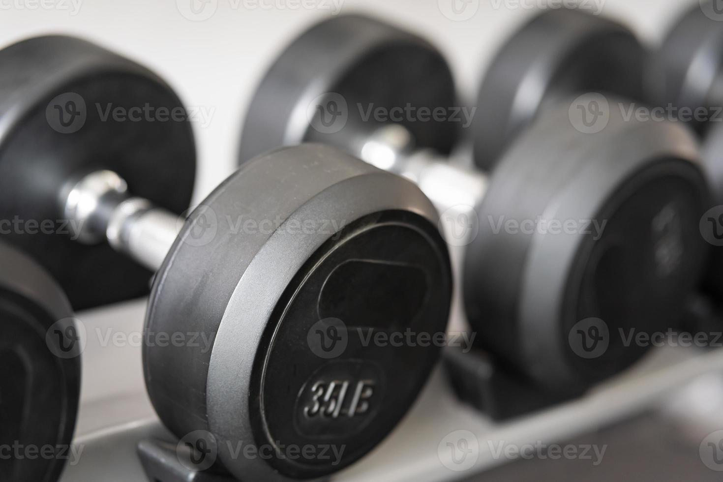 pararse con pesas. Sala de deportes y fitness. equipo de entrenamiento con pesas. juego de mancuernas negras, muchas mancuernas en el rack en el gimnasio deportivo foto