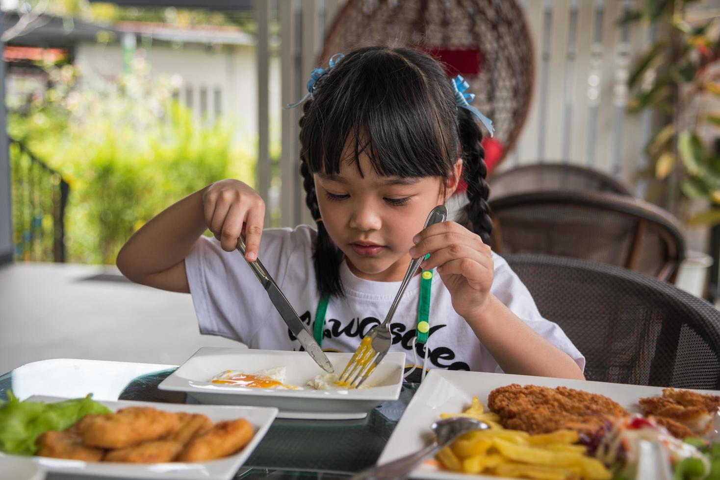 little girl asian eat fried egg on dish at table. photo