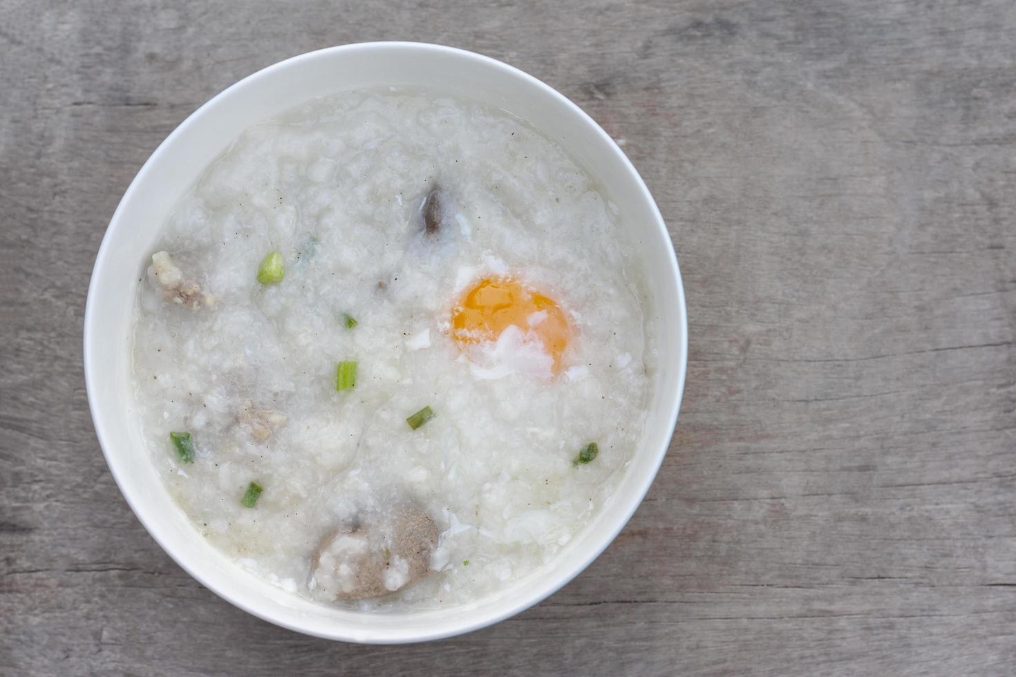 Top view of rice porridge or congee with egg in white bowl on vintage wooden table background. photo