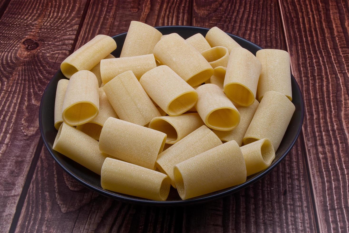 Traditional Italian uncooked Paccheri Pasta from Gragnano on wooden table. photo