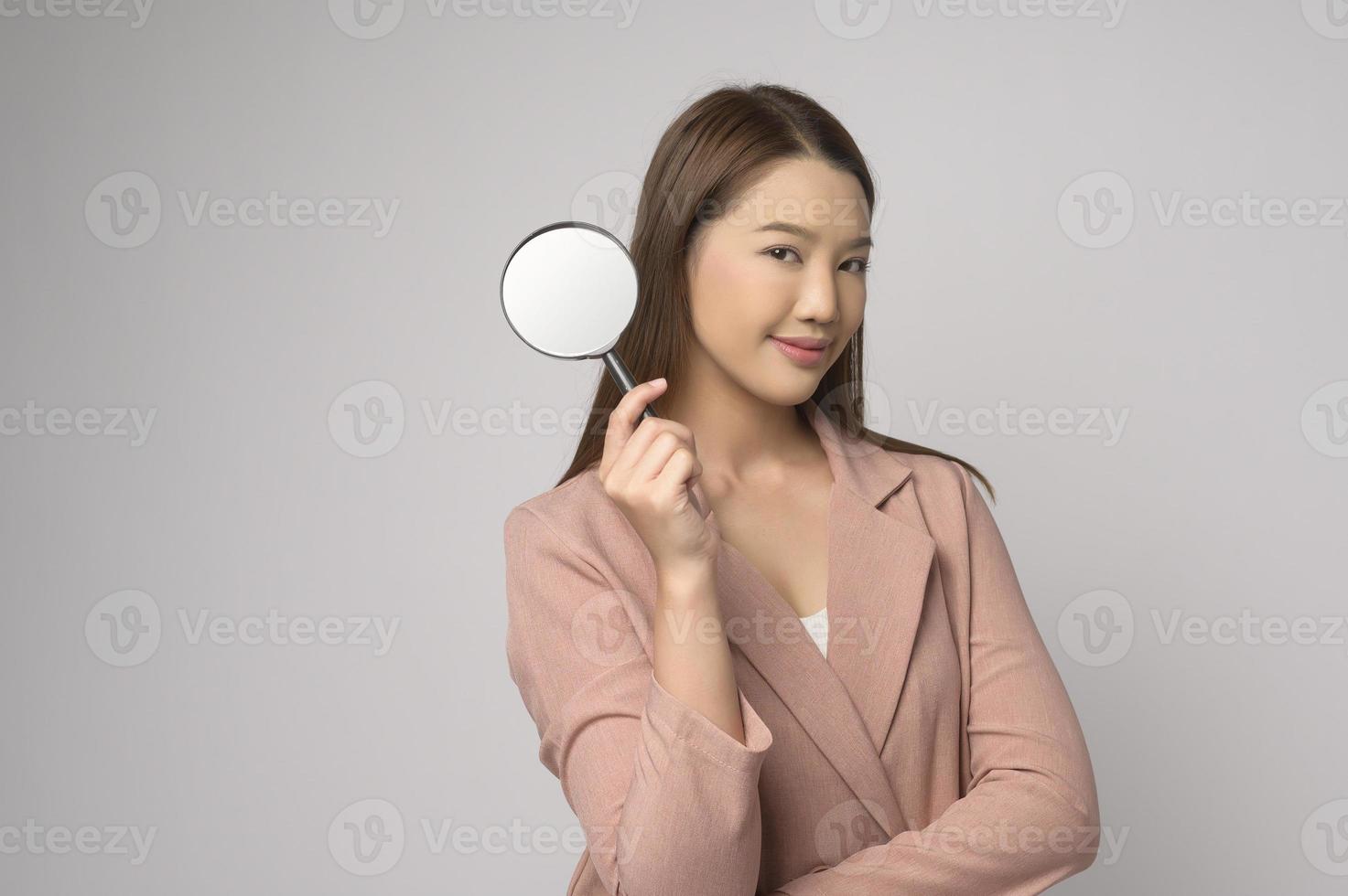 mujer asiática joven que sostiene la lupa sobre el concepto blanco del fondo, del análisis y de las finanzas. foto