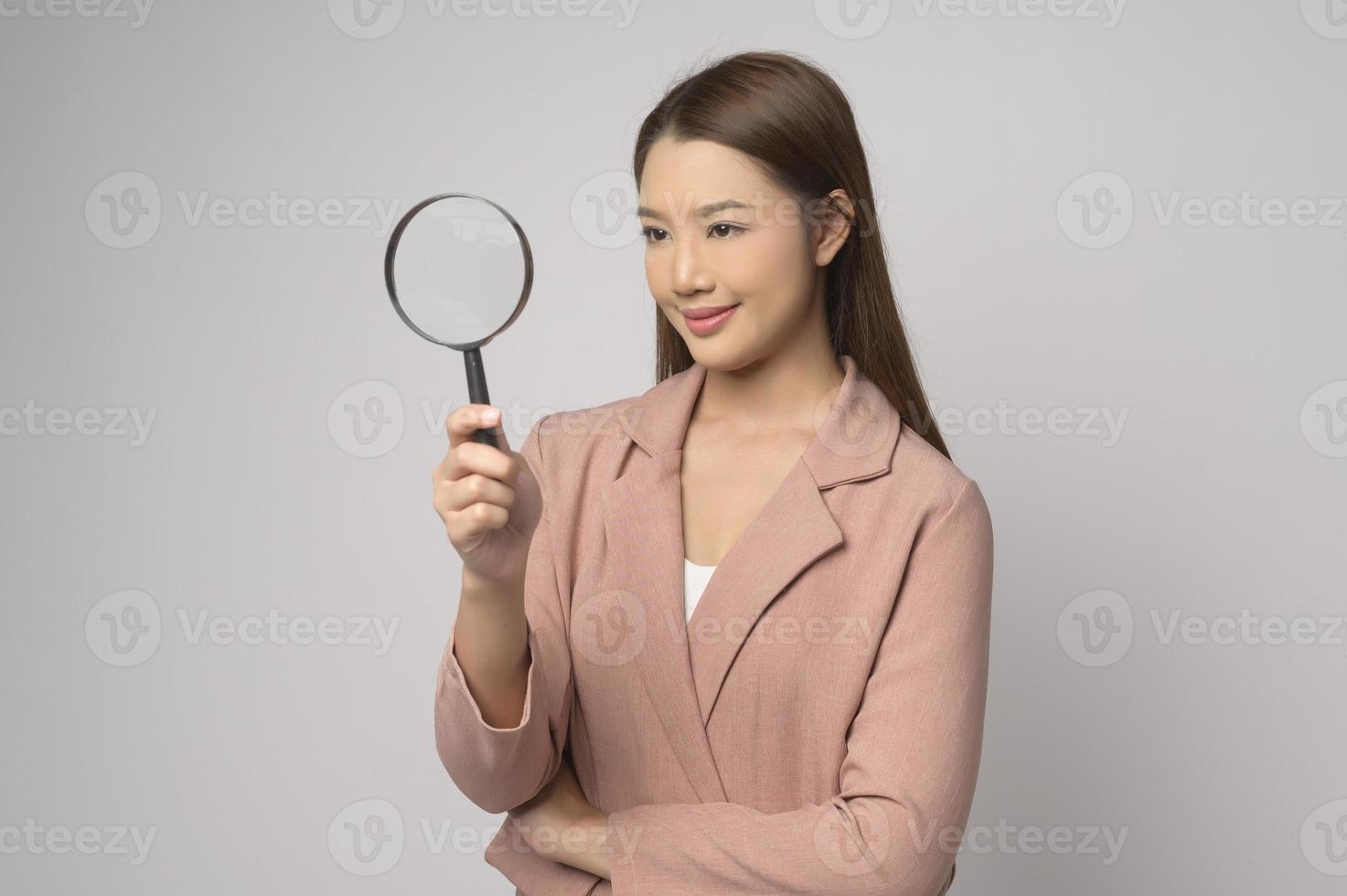 Young asian woman holding magnifying glass over white background, analysis and finance concept. photo