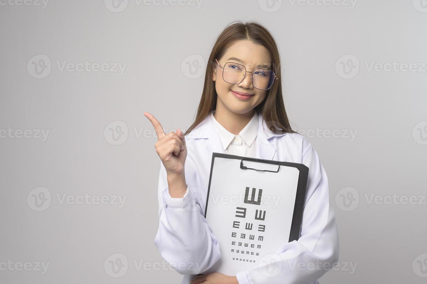 Young female ophthalmologist with glasses holding eye chart over blue background studio, healthcare concept photo