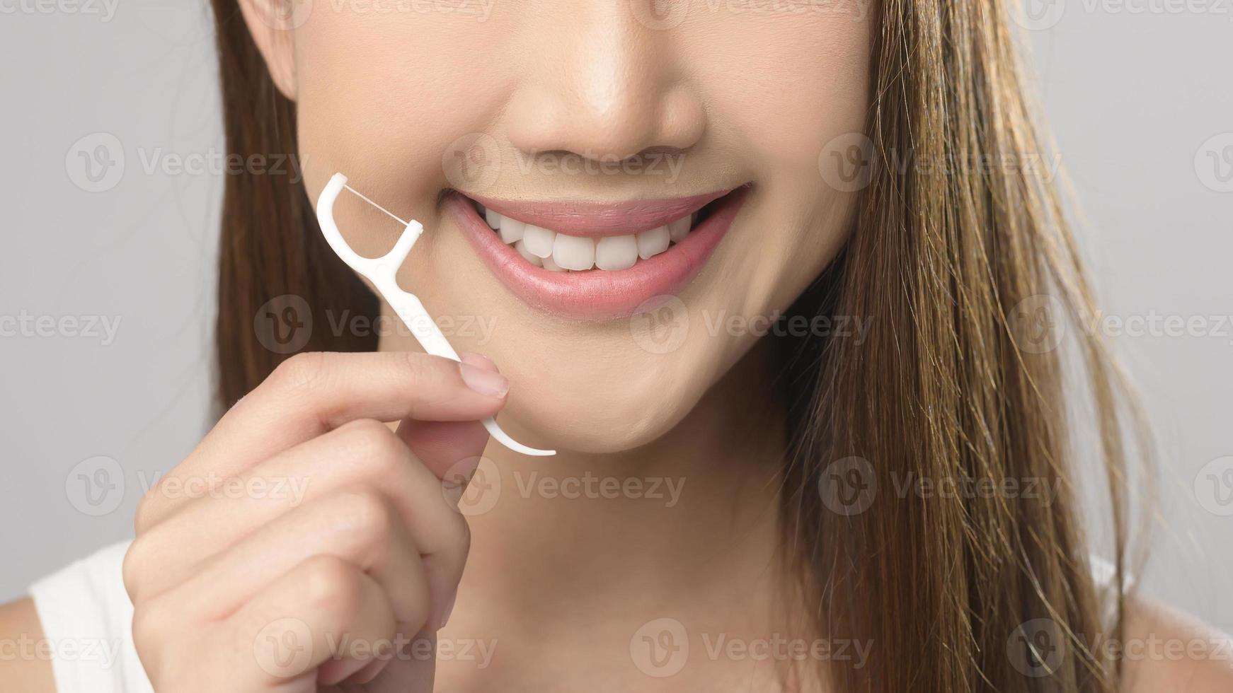 Young smiling woman holding dental floss over white background studio, dental healthcare and Orthodontic concept. photo