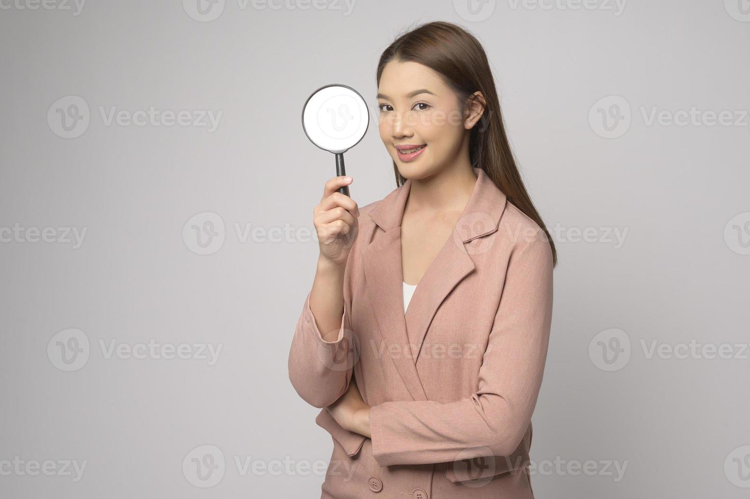 Young asian woman holding magnifying glass over white background, analysis and finance concept. photo