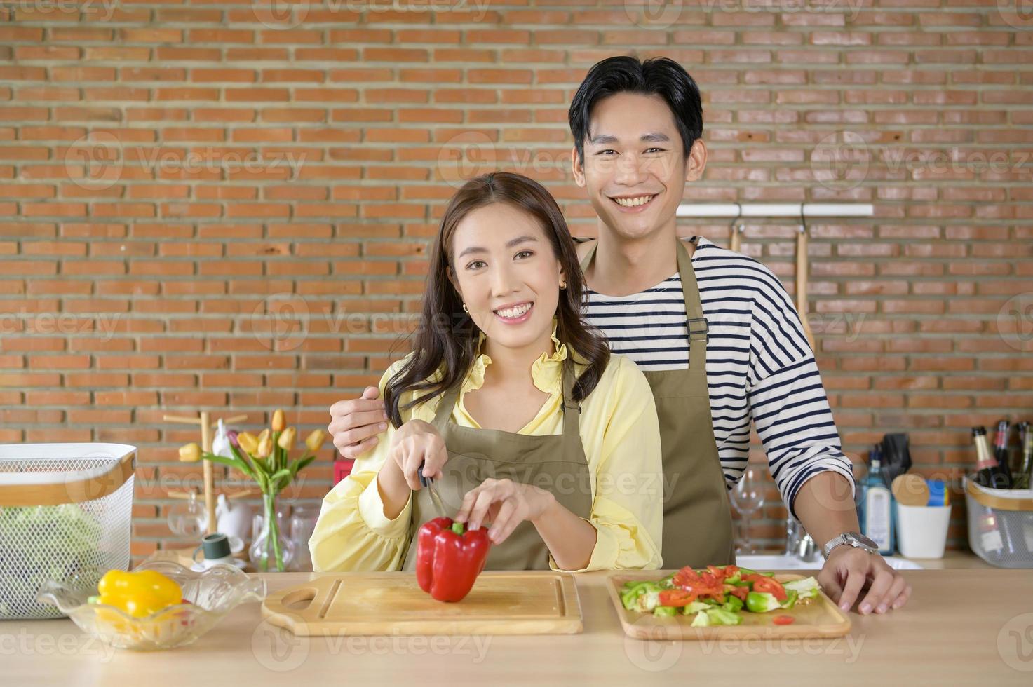 Young smiling asian couple wearing an apron in the kitchen room, cooking concept photo