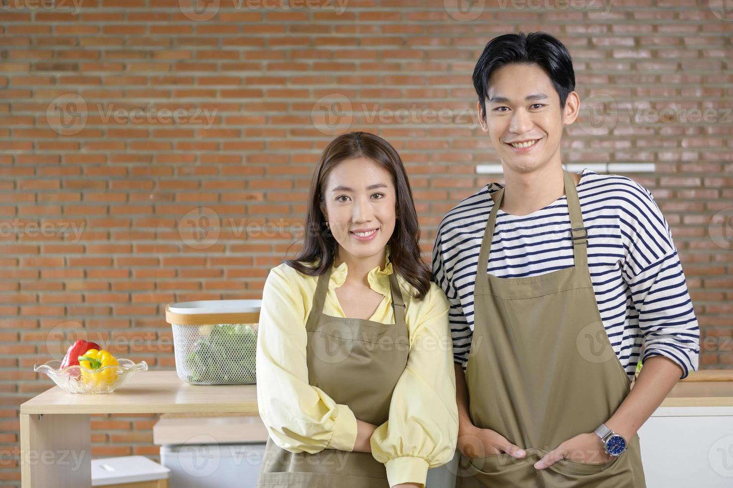 joven pareja asiática sonriente con un delantal en la cocina, concepto de cocina foto