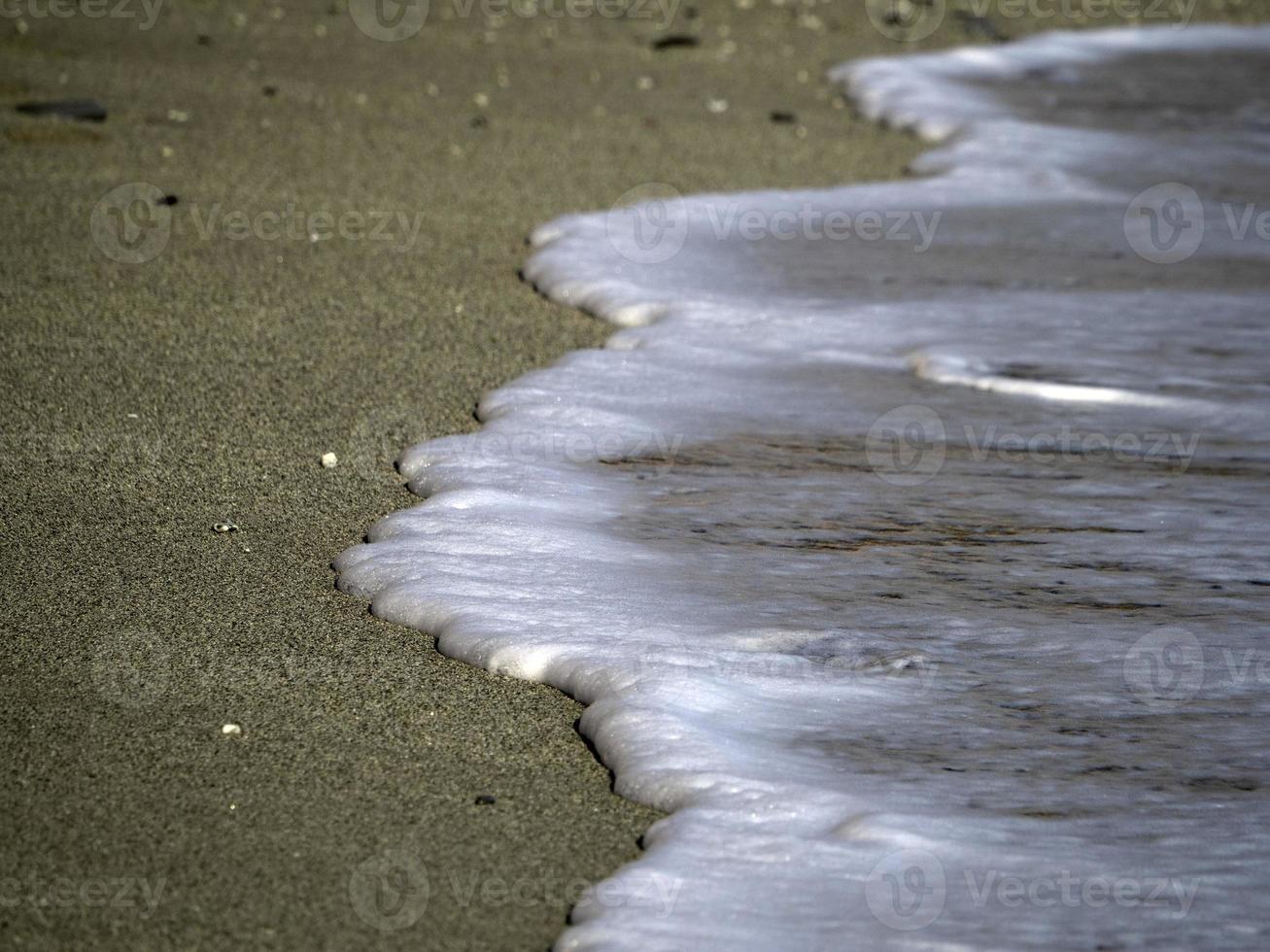 Sea wave foam on the sand beach shore photo