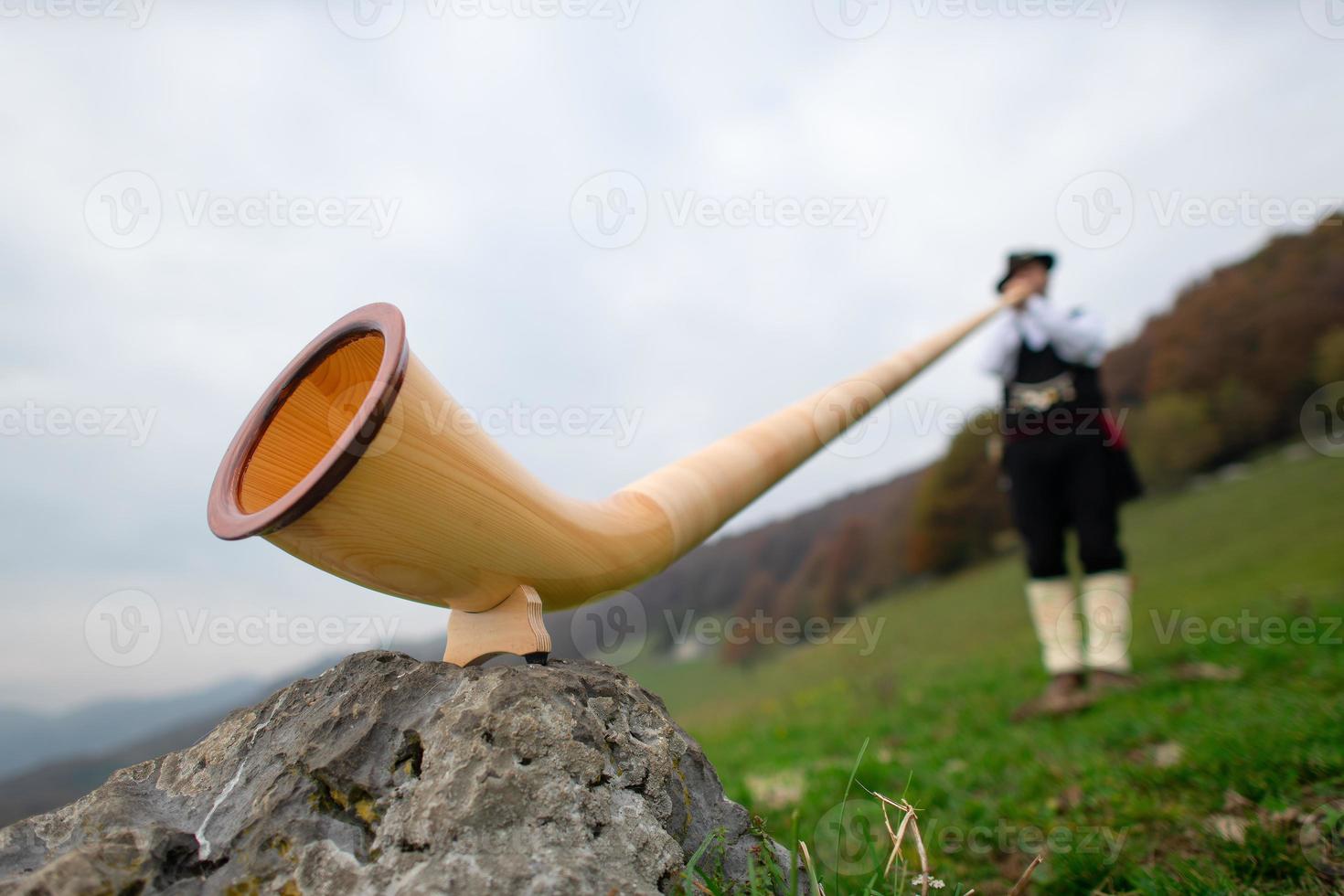 Alpine horn. A man plays in an alpine valley photo