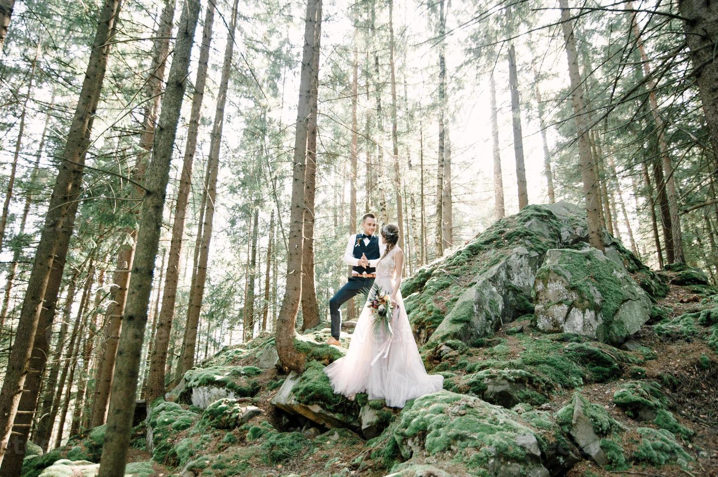 Attractive couple newlyweds, happy and joyful moment. Man and woman in festive clothes sit on the stones near the wedding decoration in boho style. Ceremony outdoors. photo