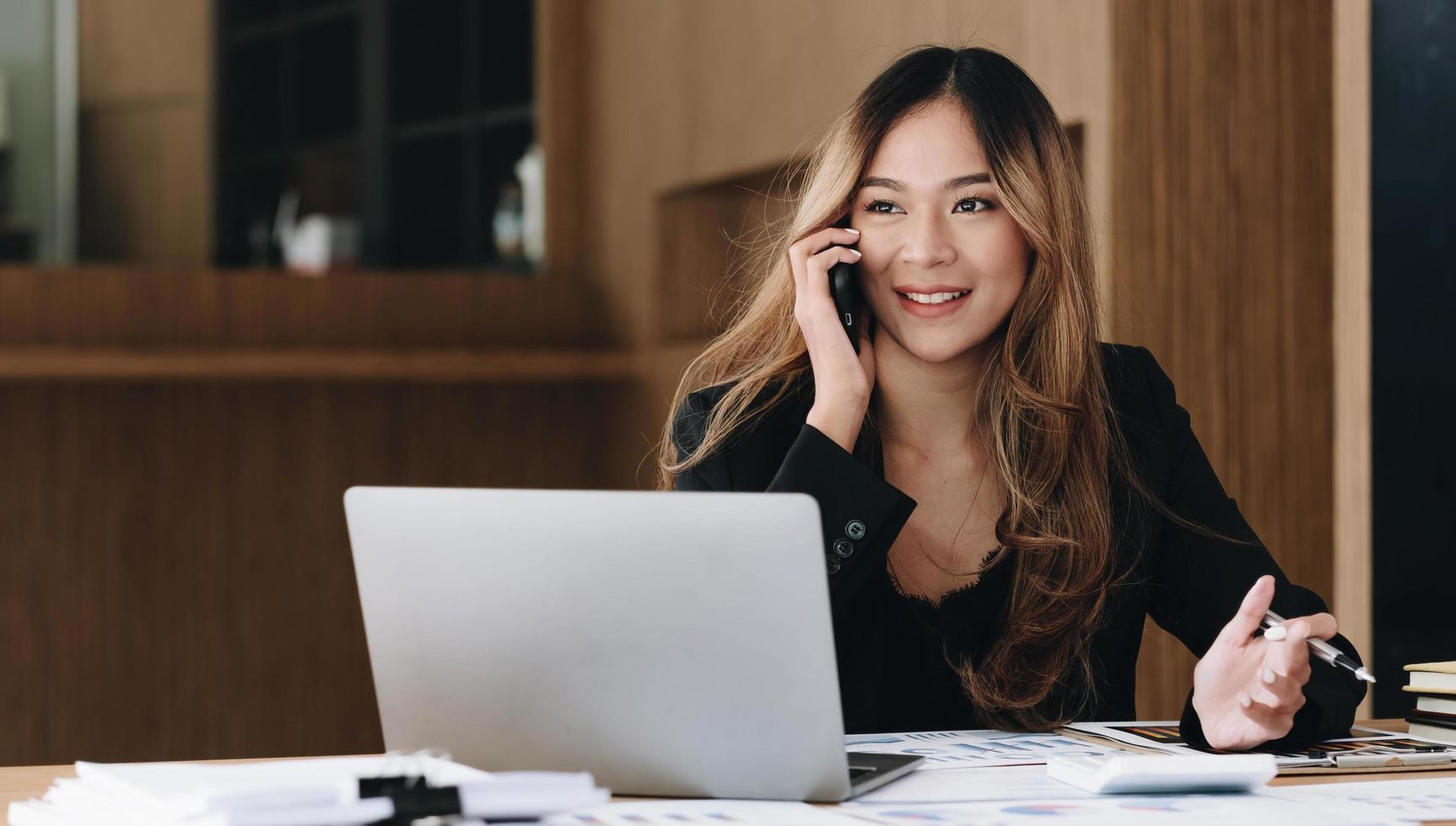 mujer de negocios asiática tiene la alegría de hablar por teléfono, computadora portátil y tableta en el escritorio de la oficina. foto