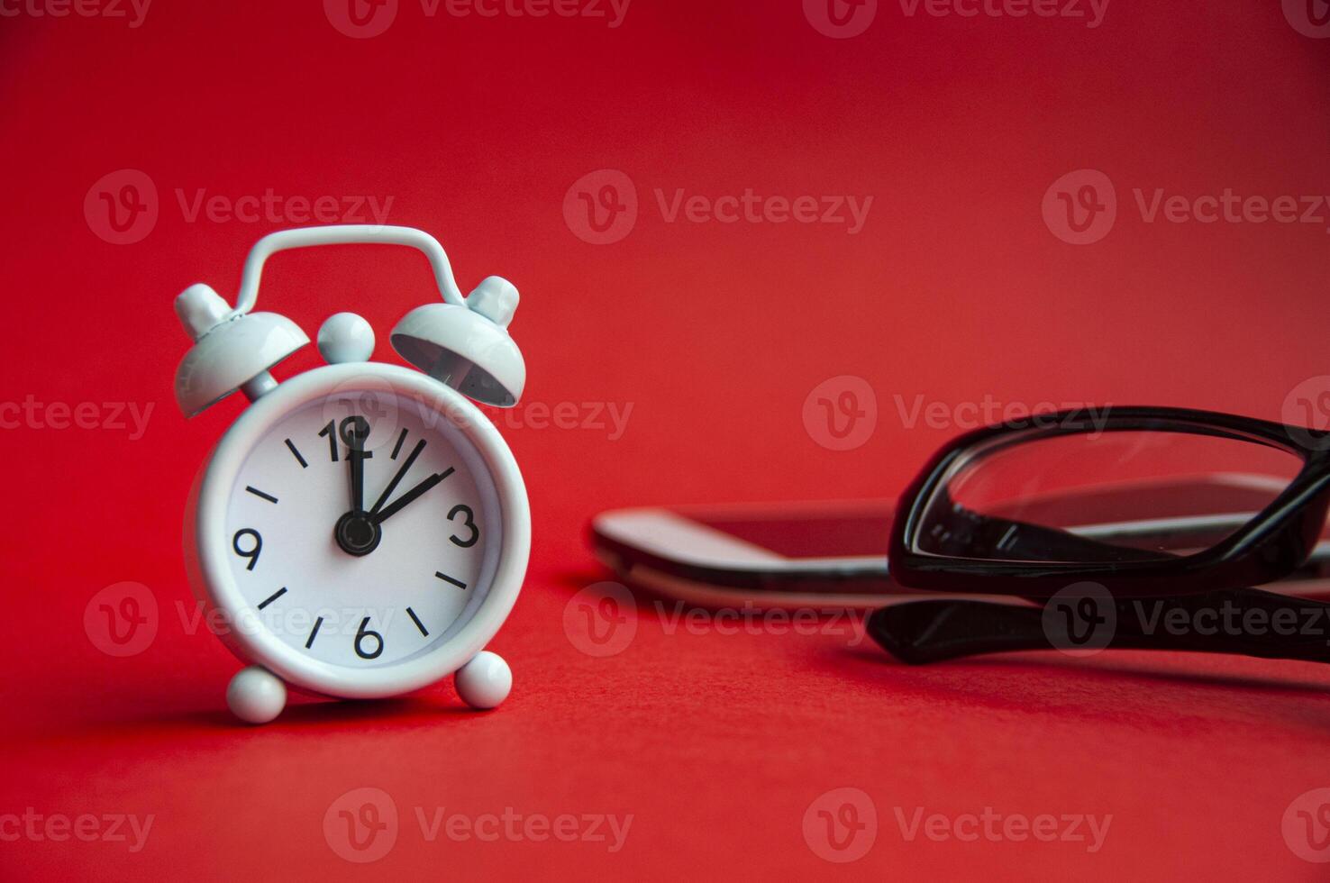 Alarm clock pointing at 2 o'clock with glasses and phone background. Copy space concept photo