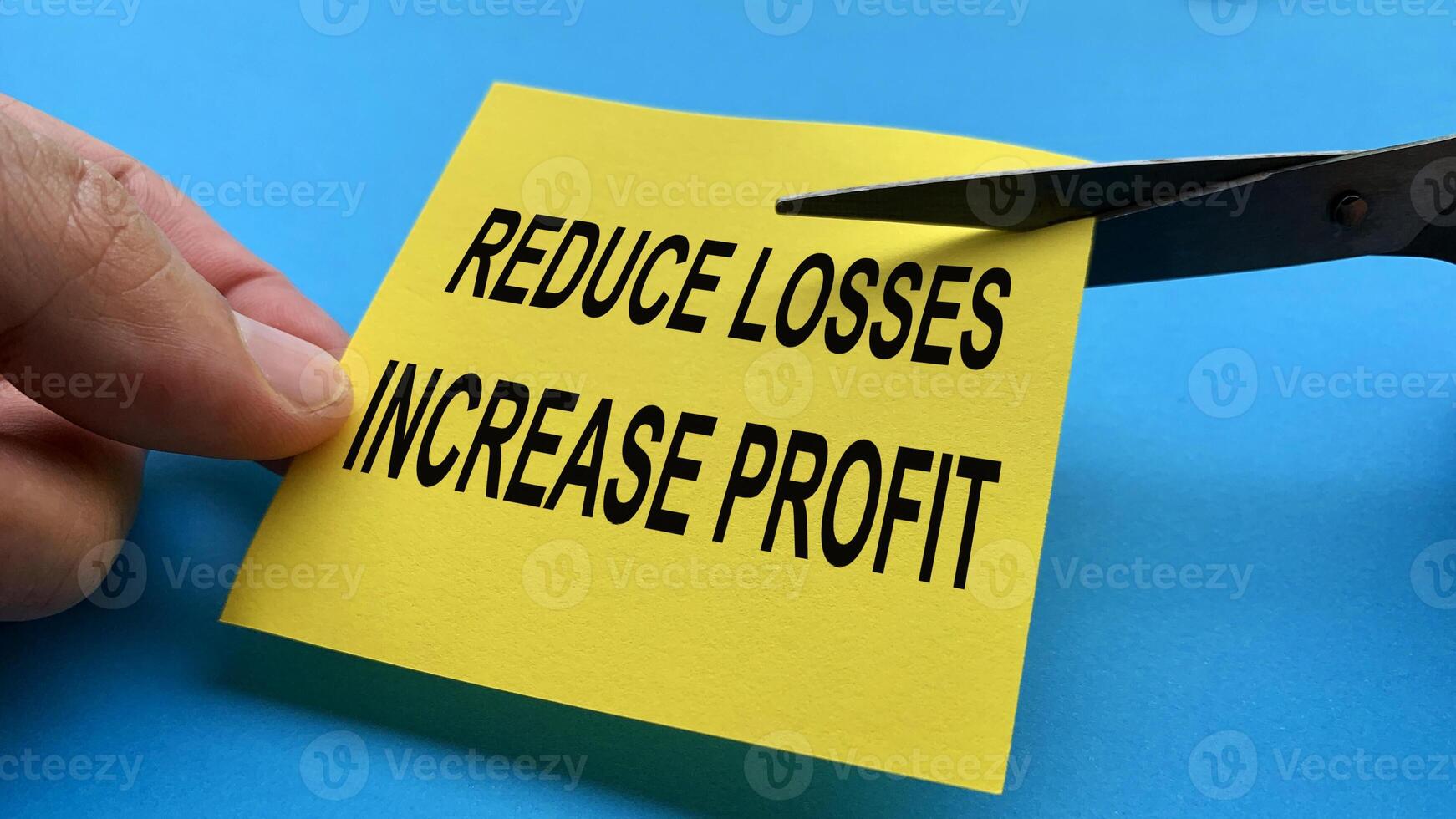Scissors that cut yellow notepad with reduce losses increase profit text on blue background. Spending concept photo