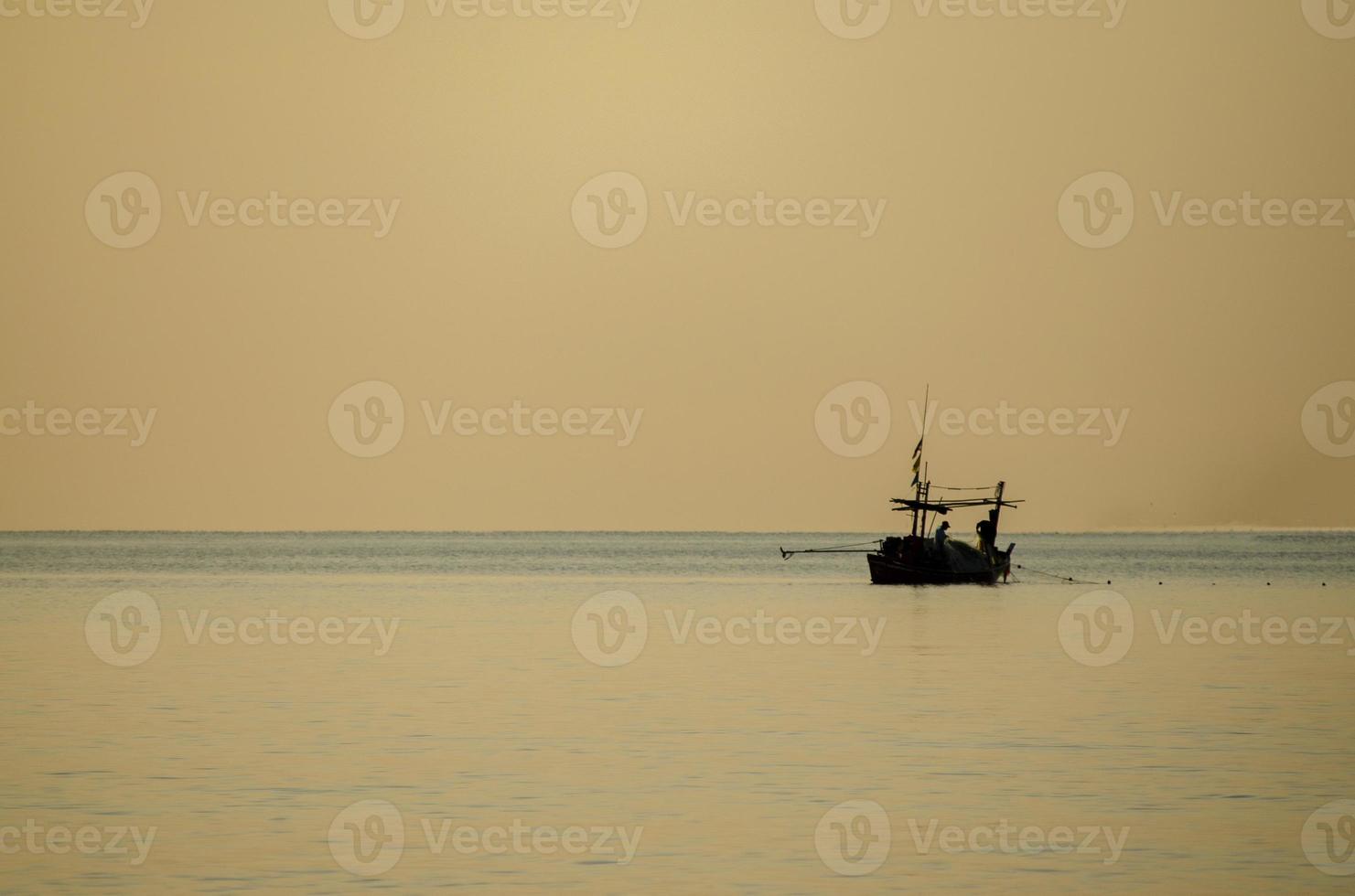 Silhouette of fishermen collecting fishing gear on a small fishing boat. The sea in the sunrise. Golden hour. photo