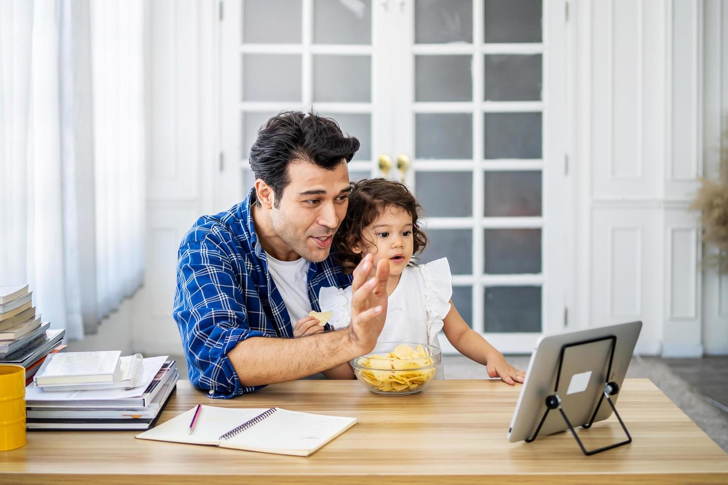 joven padre atractivo y pequeña hija linda en línea junto con su madre en videoconferencia con tableta digital para una conversación en línea en videollamada para distanciamiento social foto