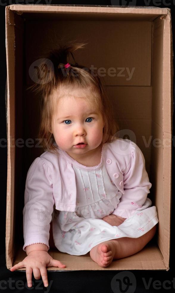 Little cute, beautiful girl sits in a box. photo