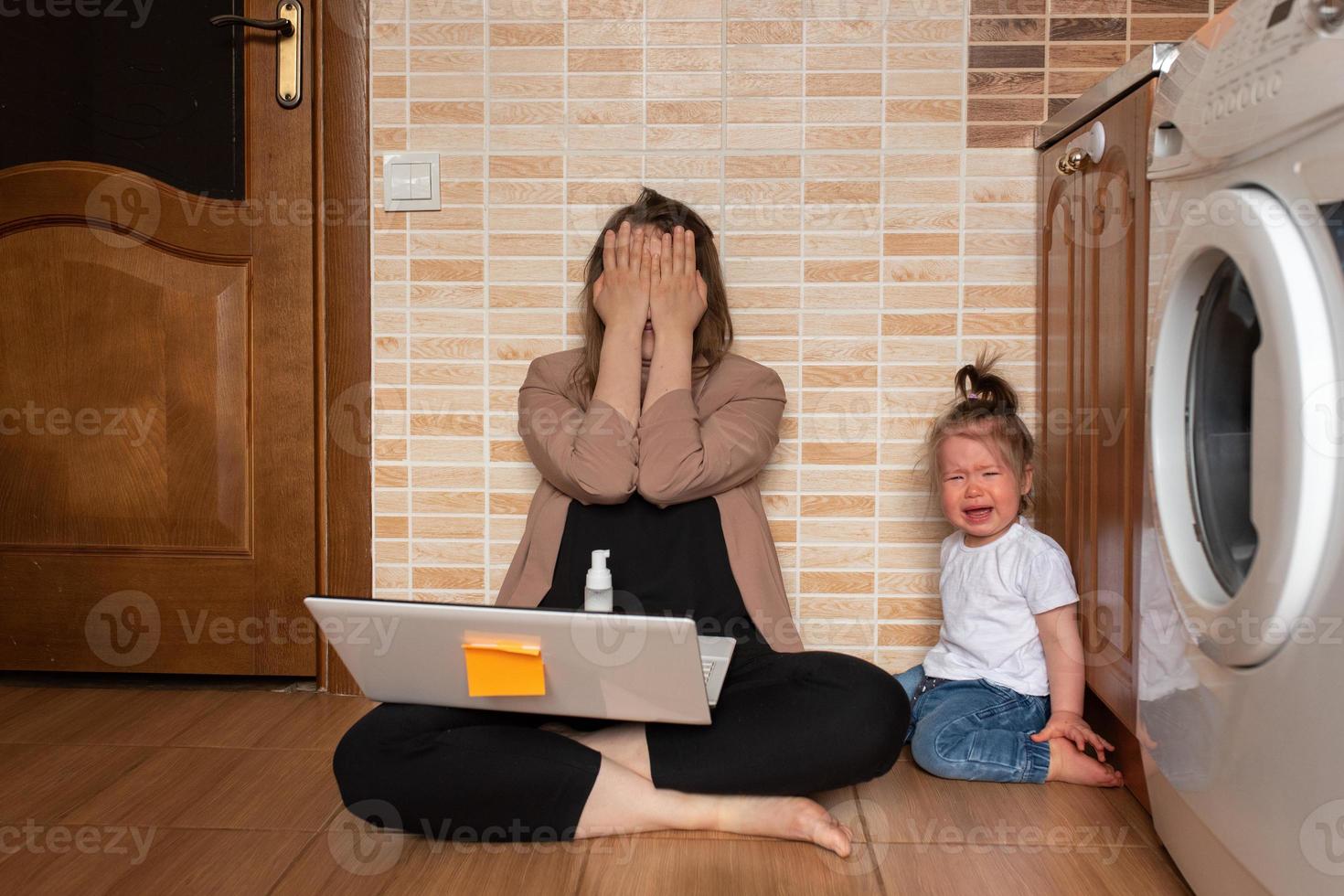 Young beautiful mother is trying to work remotely. Her little daughter is bothering her. photo