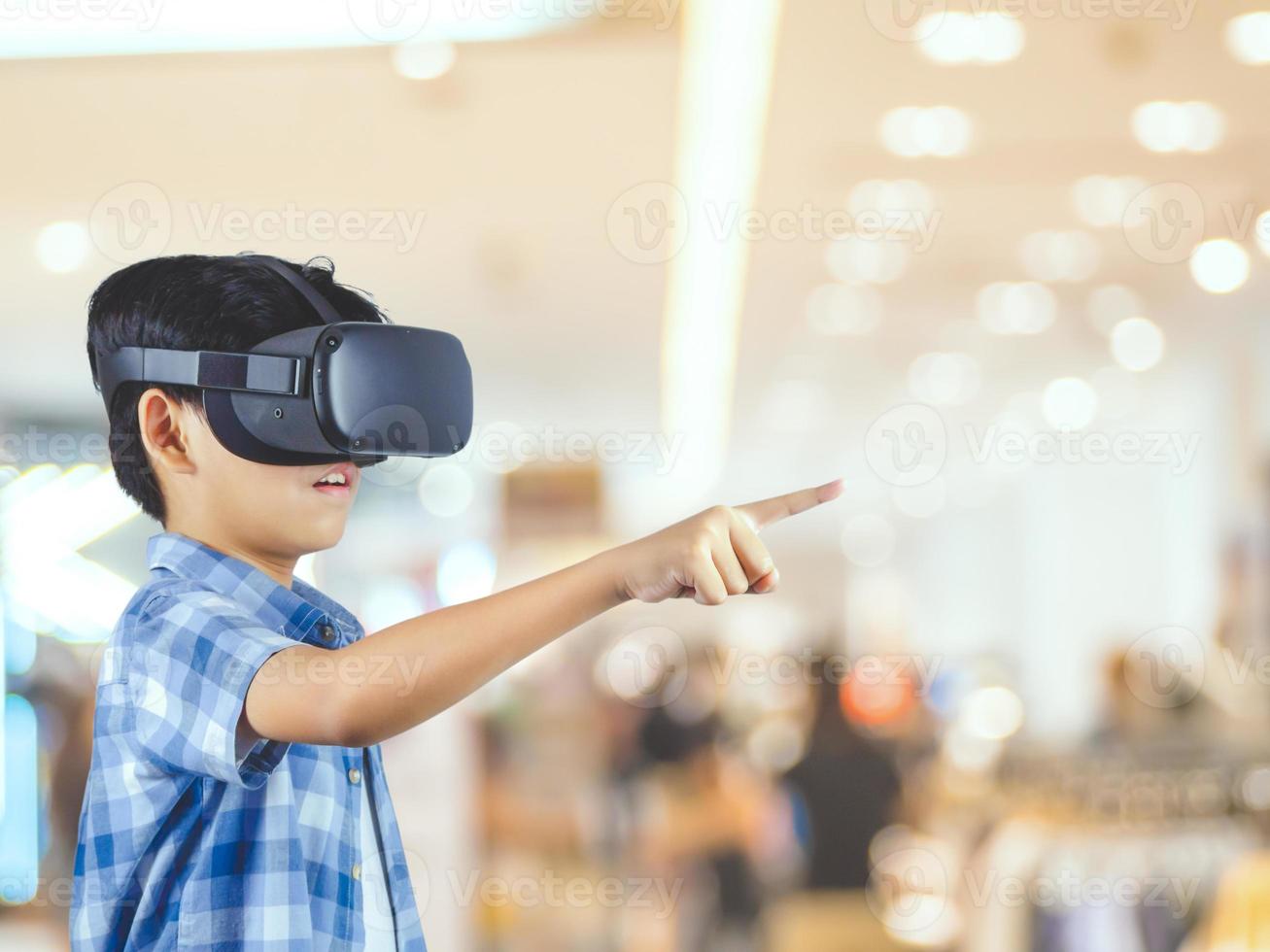 Boy wearing virtual reality glasses in modern interior design studio and trying to touch dots network and earth map or something appear in VR with exciting.Flares effect, blurred background concept. photo