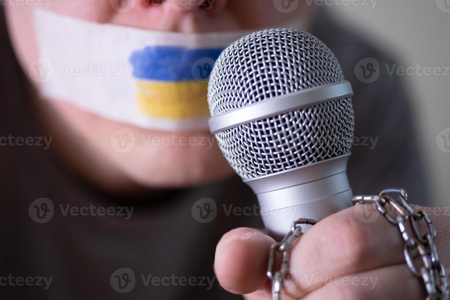 Tape over his mouth with the flag of Ukraine, trying to speak into a microphone. photo