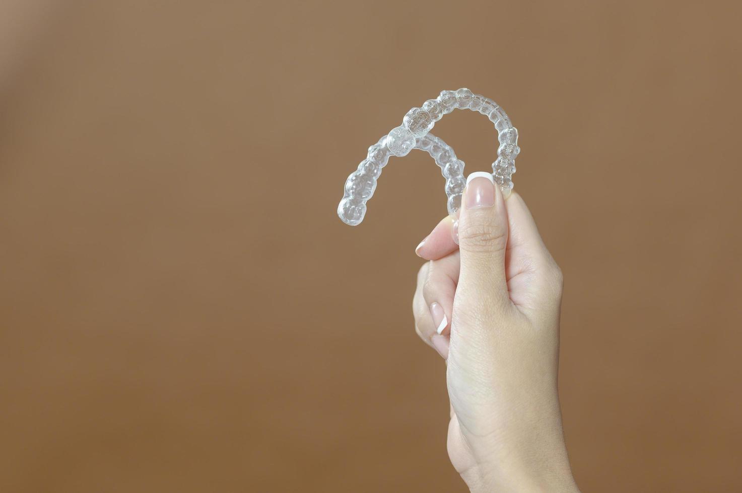 Close up young woman hand is holding Invisalign over brown background photo