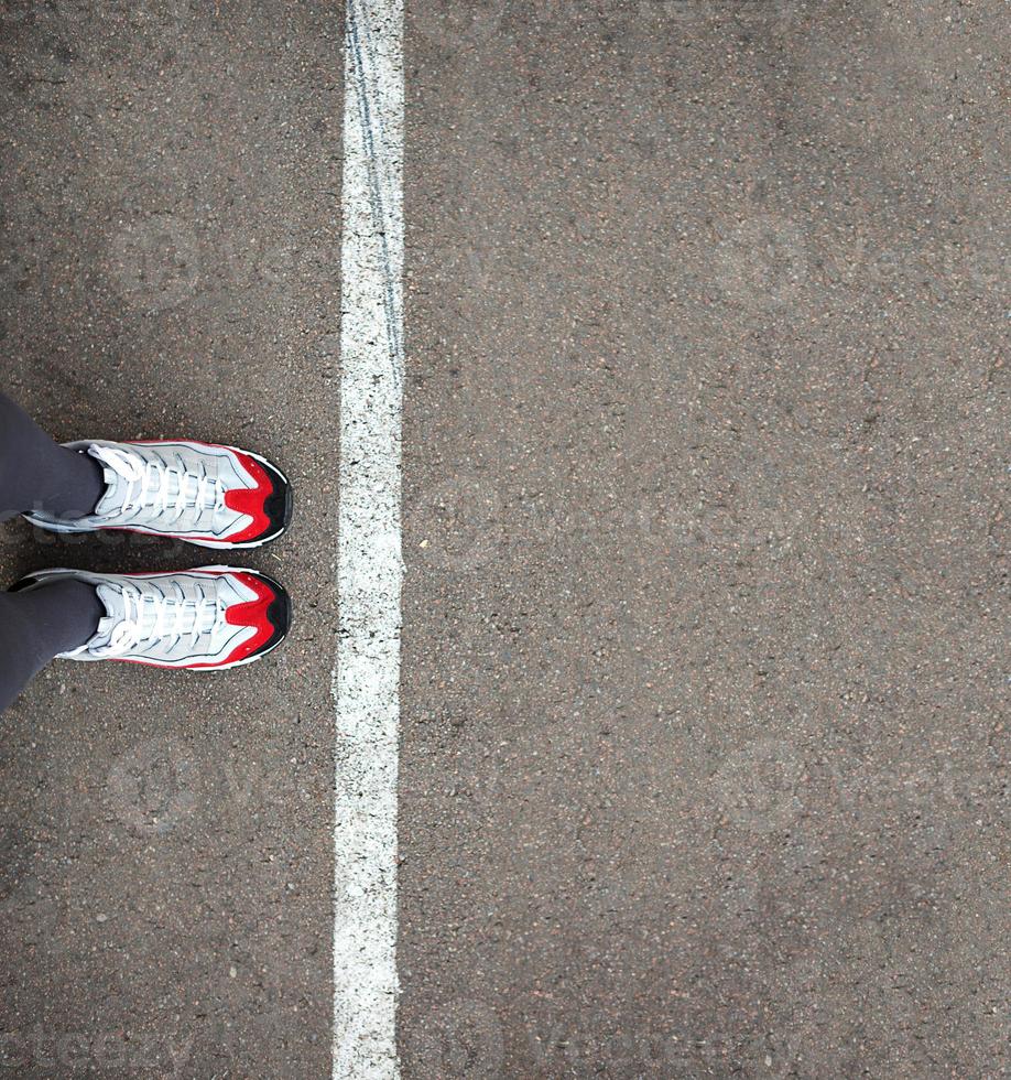 los pies en zapatillas se paran cerca de la línea divisoria en el asfalto. línea delimitadora, distancia social, esperando en línea. la frontera, haga cola para empezar. copie el espacio foto