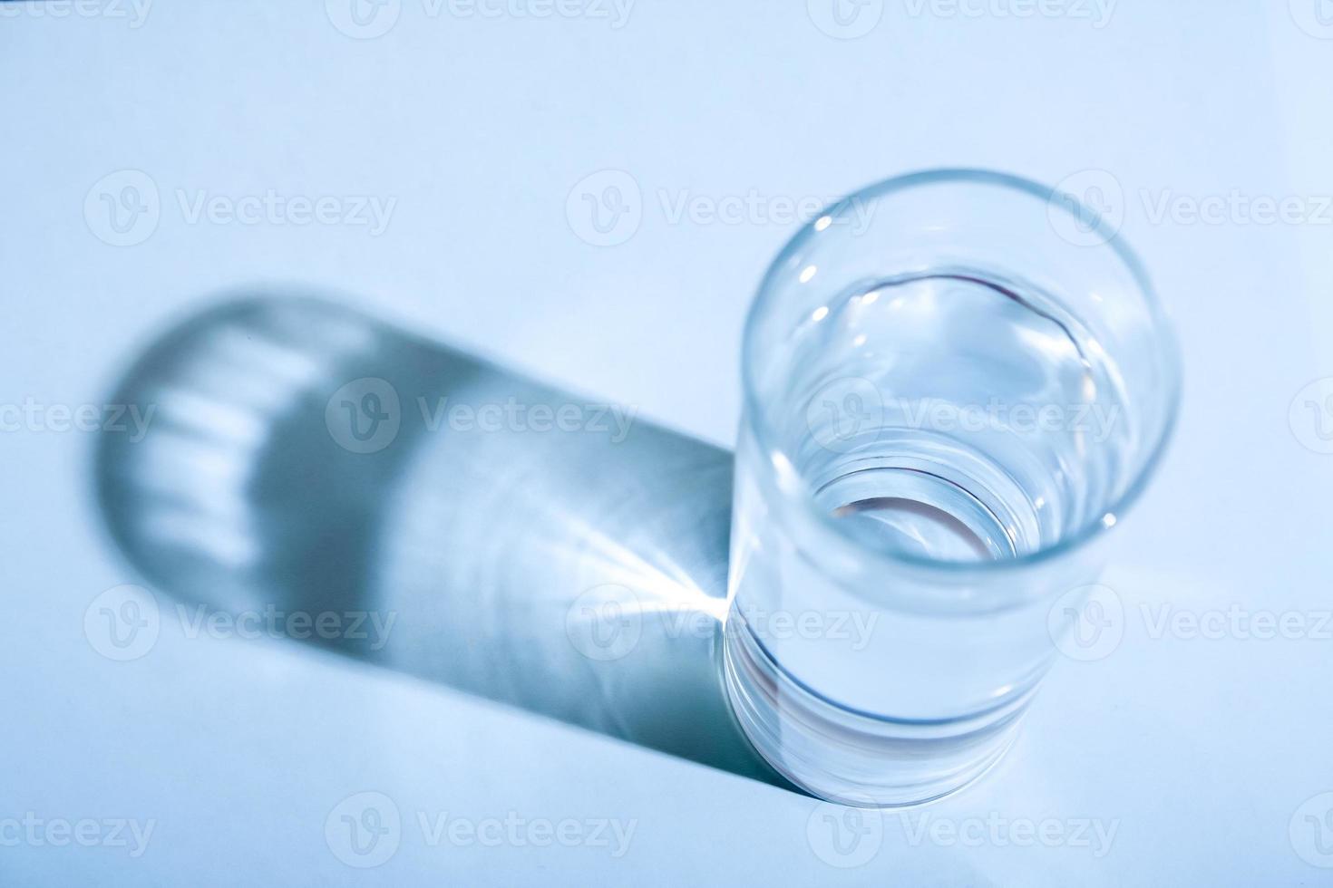 Glass of clean water with shadow in blue monochrome. photo