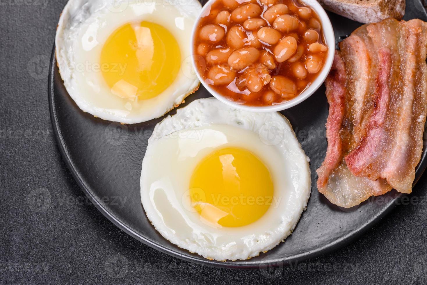 English breakfast with fried eggs, bacon, beans, tomatoes, spices and herbs photo