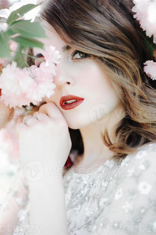 very beautiful girl the bride under a veil, beige wedding dress near the tree Sakura is looking down, nature photo