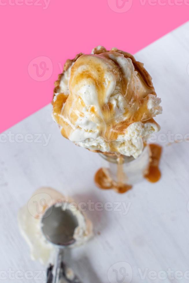 melting vanilla ice cream scoops with dripping caramel sauce over waffle cone on fun vibrant pink background photo