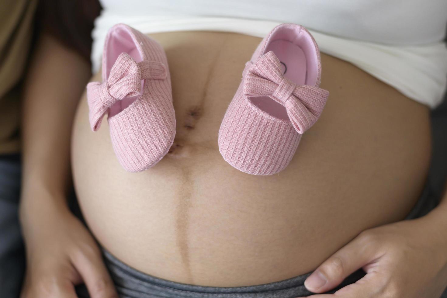 joven embarazada poniendo zapatos de bebé en el concepto de cuidado de la barriga, la familia y el embarazo foto