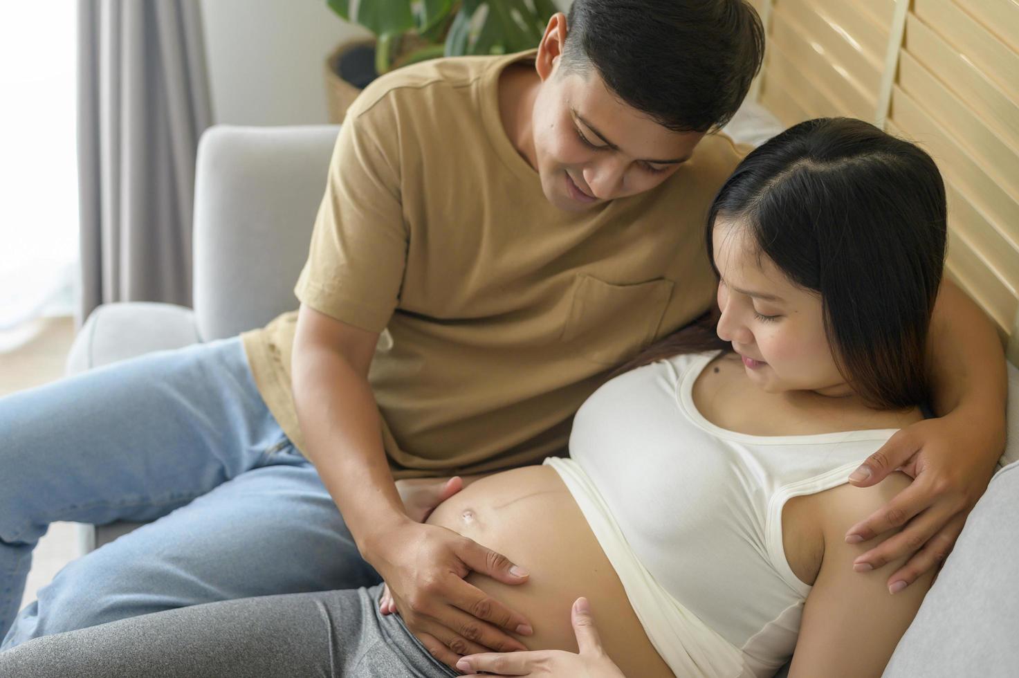 Young pregnant woman with husband embracing and expecting a baby at home photo